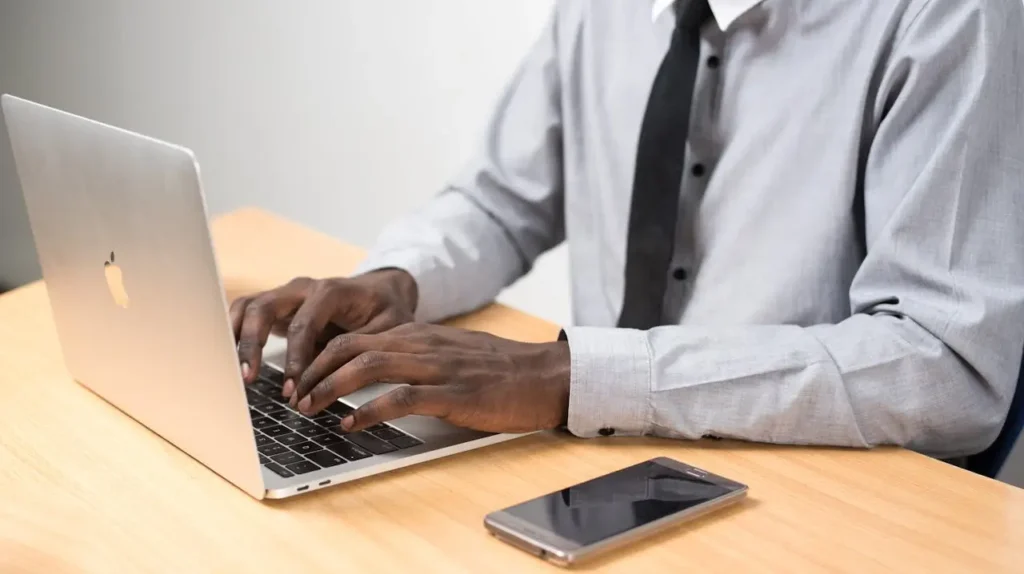 Homem digitando em laptop com smartphone ao lado
