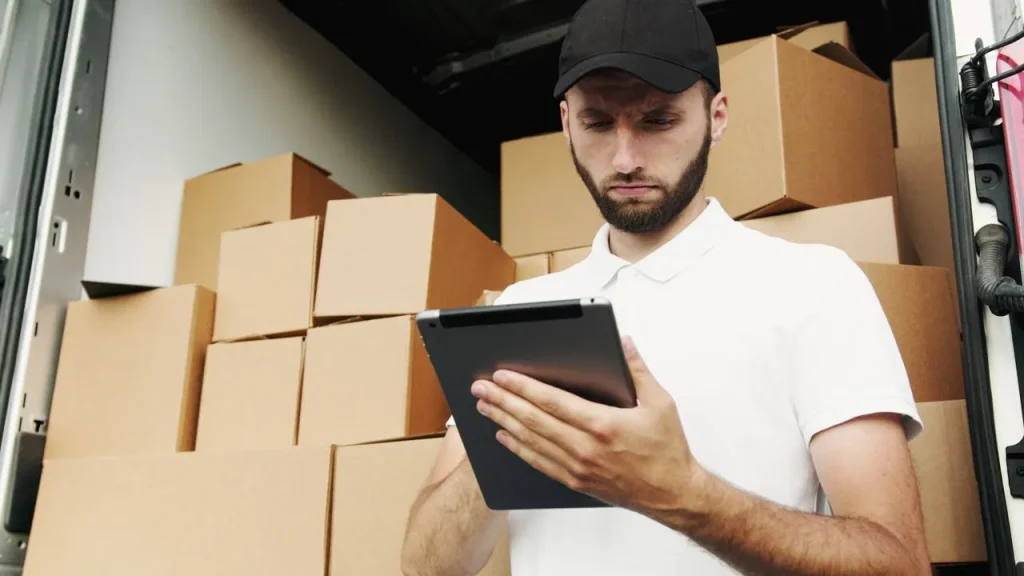 Homem com tablet em frente a caixas empilhadas.